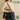 Person holding a black handbag with a cat-themed keychain, wearing a beige sweater and blue jeans, in a room with a decorative wall.