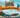 An outdoor cat festival set in a sunny park with stalls, bunting, and costumed cats. A giant balloon arch at the entrance is shaped like a cat face, and across the arch it says "500 Popular Cat Names"
