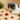 Cat playing with a wooden toy with holes containing small toys on a light-colored surface.