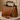 Brown leather handbag with gold handle and cat keychain on a marble surface.