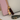 Gold cat charm with a tassel on a pink handbag and gray strap.