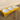 Yellow elevated pet feeder with three white bowls on a wooden floor.