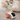 A fluffy white and beige cat is reaching toward a small robot toy with an orange wheel, black dome, gray antenna, and pastel feather wand on a beige rug.